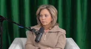 Julie Chrisley sitting in front of a green backdrop in a white chair