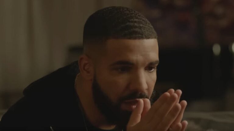 Drake sitting down with his hands folded.