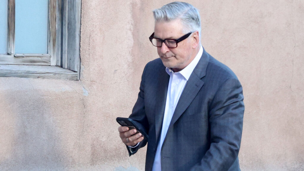 Alec Baldwin staring at his phone while pushing a baby stroller.