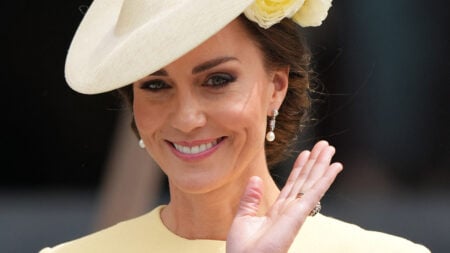 Photo of Kate Middleton waving in a cream-colored outfit and a hat.