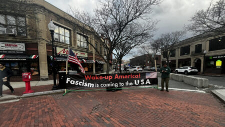 A large banner at Davis Square in Boston reads: "Wake-up America! Fascism is coming to the U.S.A."