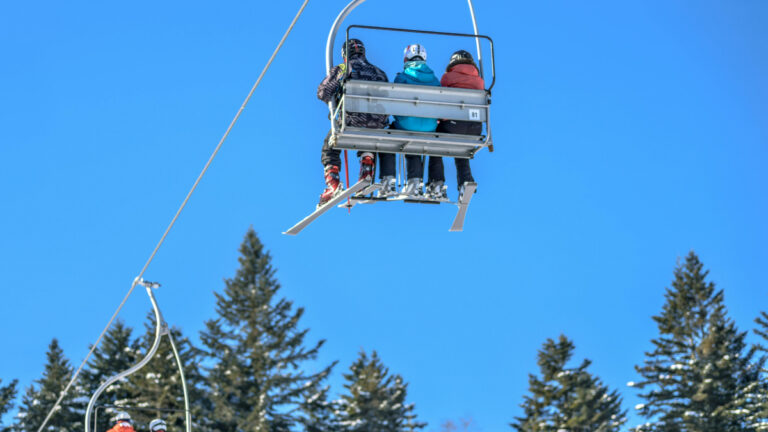 Skiers on a mountain lift with trees below them