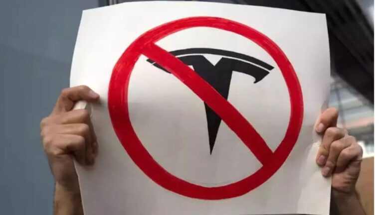 Tesla Showroom Showdown: Customer’s Test Drive Thwarted by Manhattan Protesters two hsnds holding a tesla protest sign